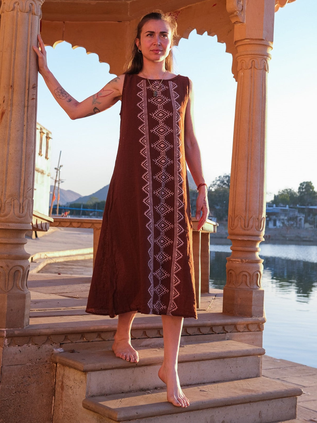 Ekakshi Maxi Dress in rust brown, model descending temple steps at dusk with a lake behind