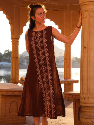 Ekakshi Maxi Dress in rust brown, model seated on carved temple steps beside a lake in golden light