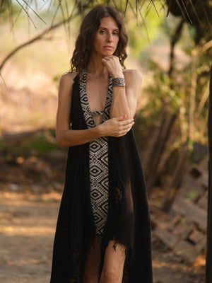 Model in black halter maxi dress, arm across, against sunlit leaves