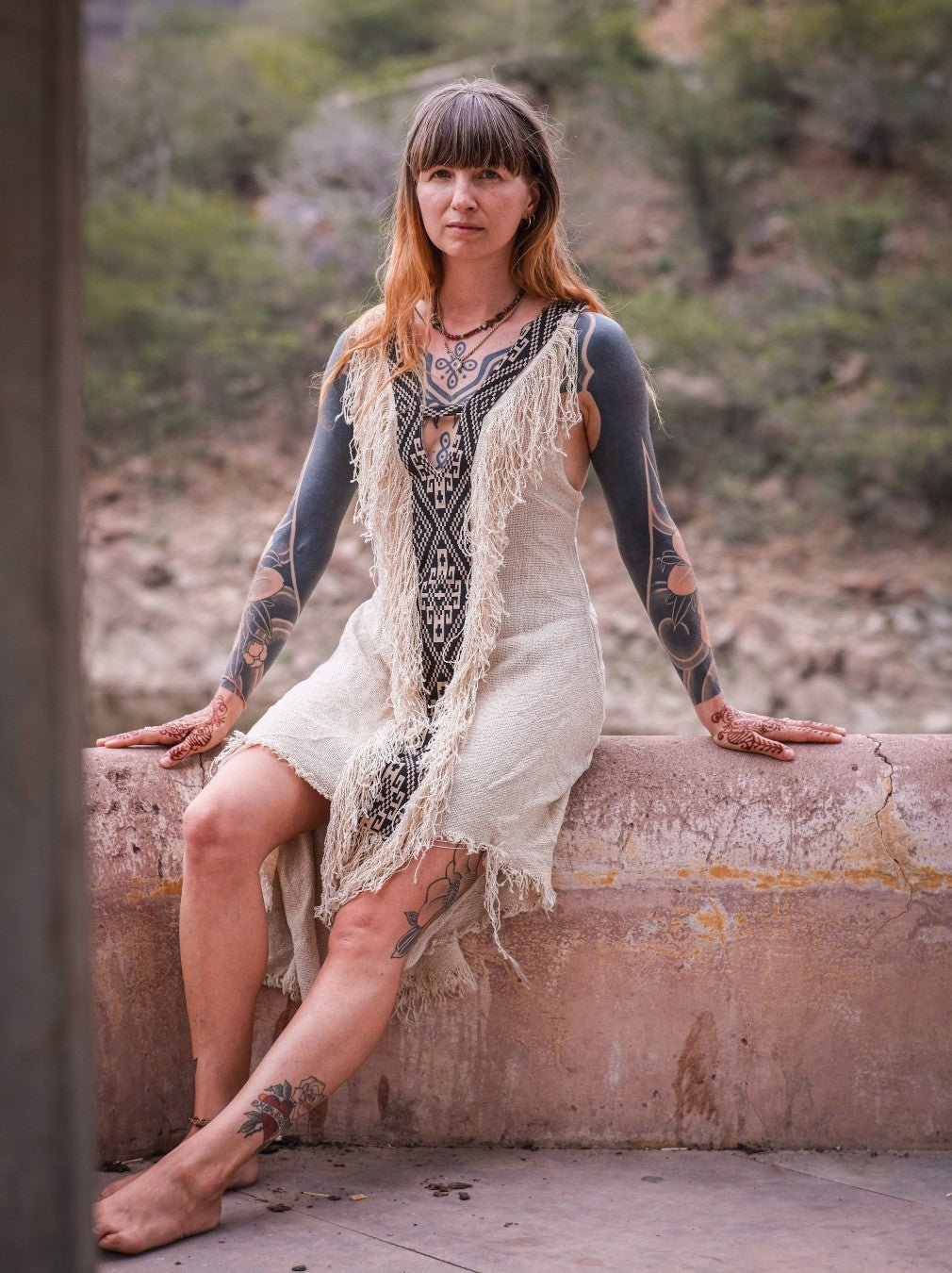 Seated model in cream fringe maxi with tribal panel, riverside heritage setting