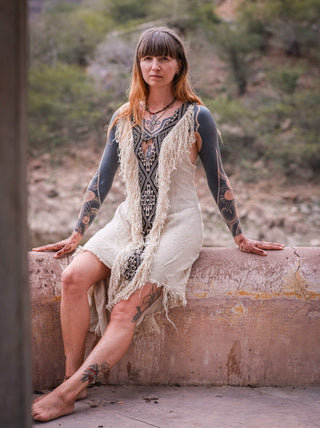 Seated model in cream fringe maxi with tribal panel, riverside heritage setting