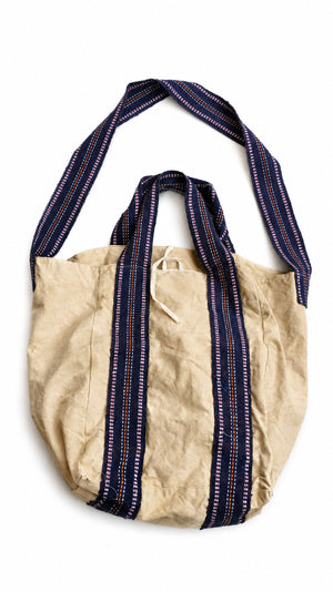 The Anoop Tote Bag, crafted from beige cotton canvas with navy blue and white striped handles and a coordinating long shoulder strap, is displayed against a white background — the perfect everyday shoulder bag for casual outings.