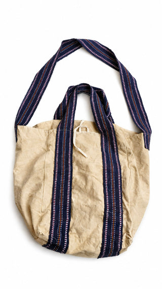The Anoop Tote Bag, crafted from beige cotton canvas with navy blue and white striped handles and a coordinating long shoulder strap, is displayed against a white background — the perfect everyday shoulder bag for casual outings.