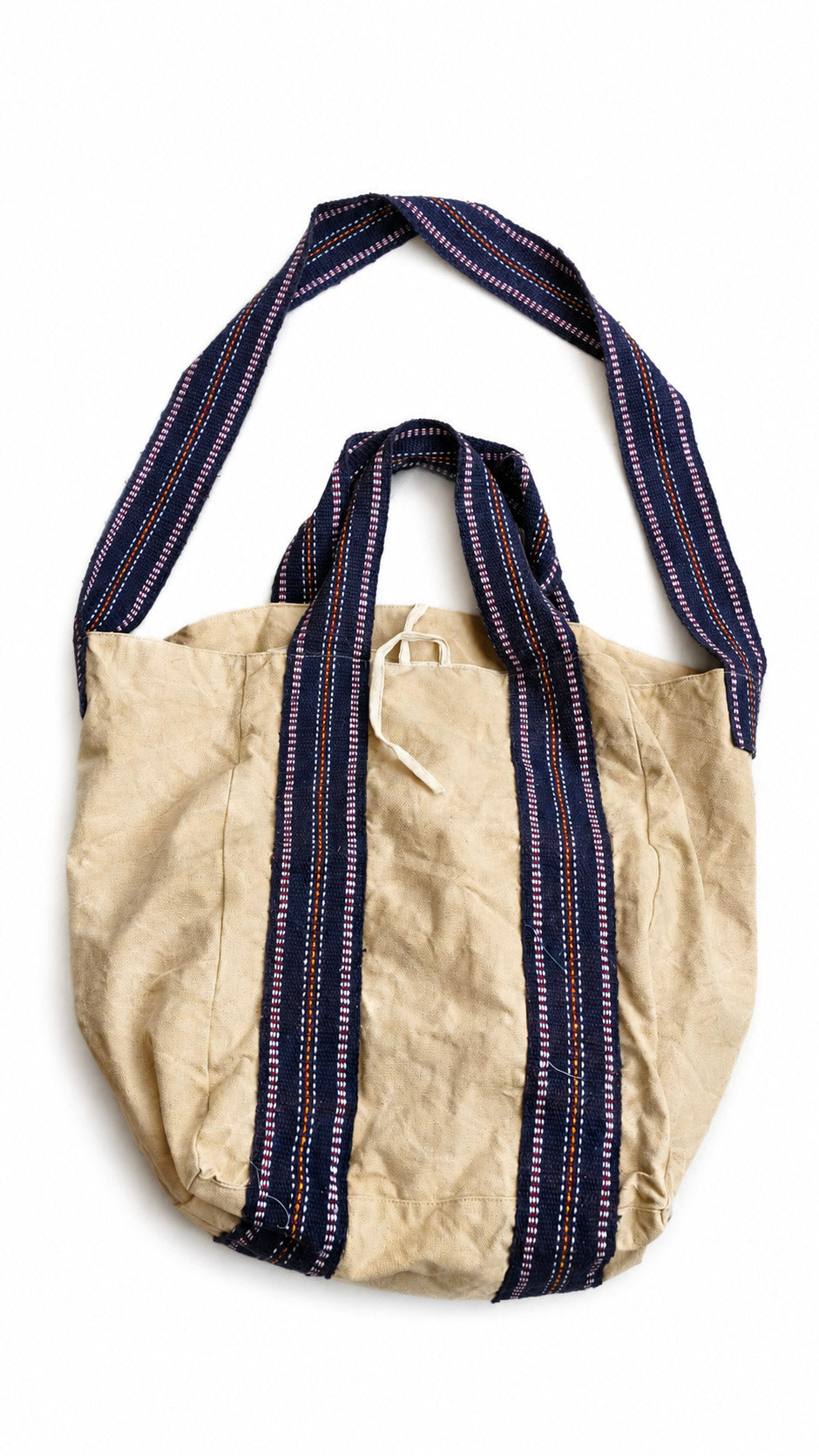 The Anoop Tote Bag, crafted from beige cotton canvas with navy blue and white striped handles and a coordinating long shoulder strap, is displayed against a white background — the perfect everyday shoulder bag for casual outings.