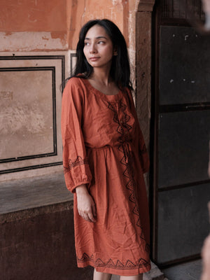 Gerua terracotta A-line cotton dress modelled on a Rajasthan street, showing the buttoned placket and waist tie