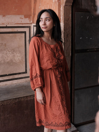 Gerua terracotta A-line cotton dress modelled on a Rajasthan street, showing the buttoned placket and waist tie