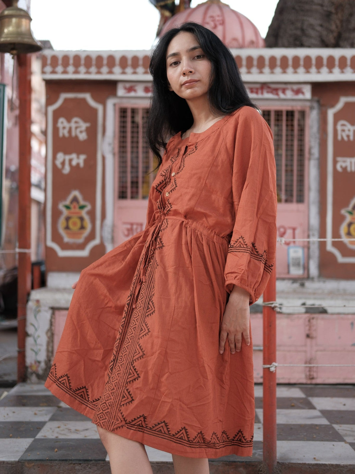 Gerua rust cotton dress for women worn before a pink Rajasthani temple in a knee-length A-line silhouette