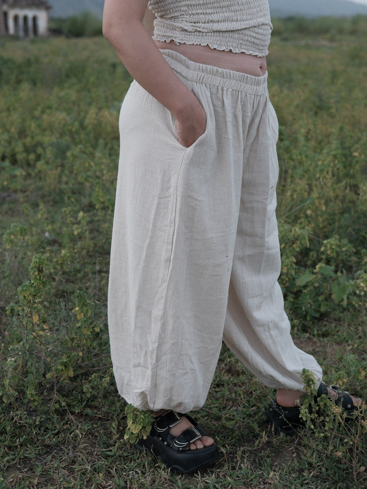 Side view of Hoor ivory khadi harem pants mid-stride, the wide leg falling to a gathered ankle cuff in tall grass