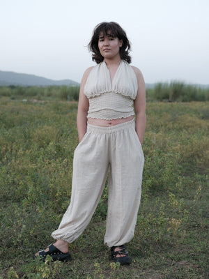 Model wearing Hoor unisex ivory khadi cotton harem pants with a smocked halter top, standing in an open field