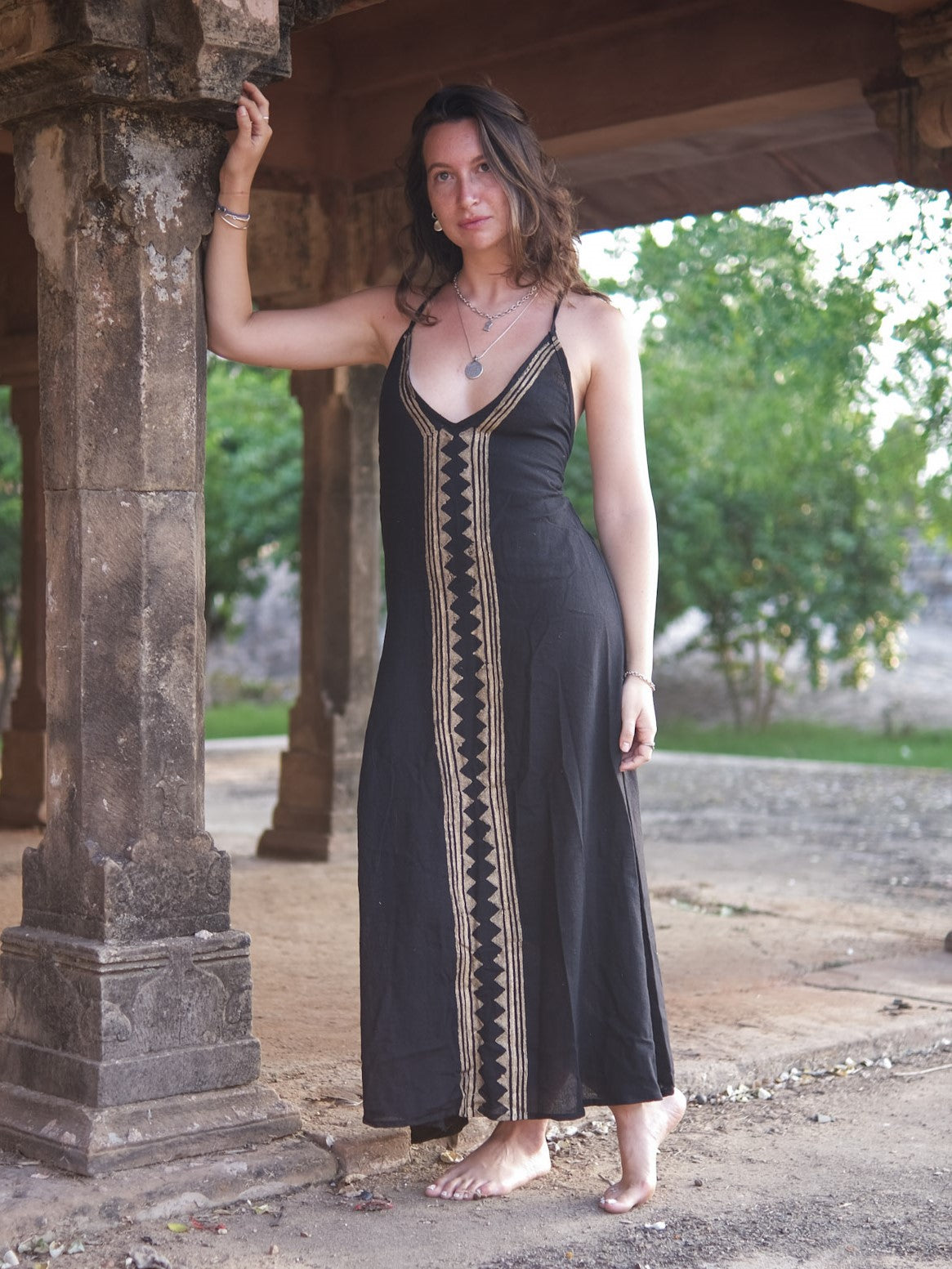 Idhika Dress in black, front view of the free-size cotton maxi beside a pillar and trees