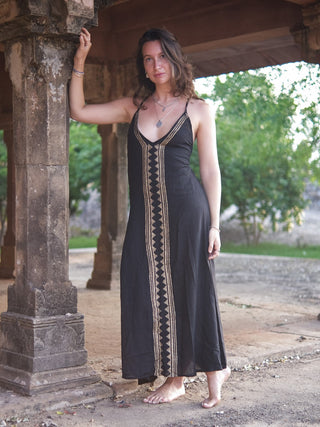 Idhika Dress in black, front view of the free-size cotton maxi beside a pillar and trees