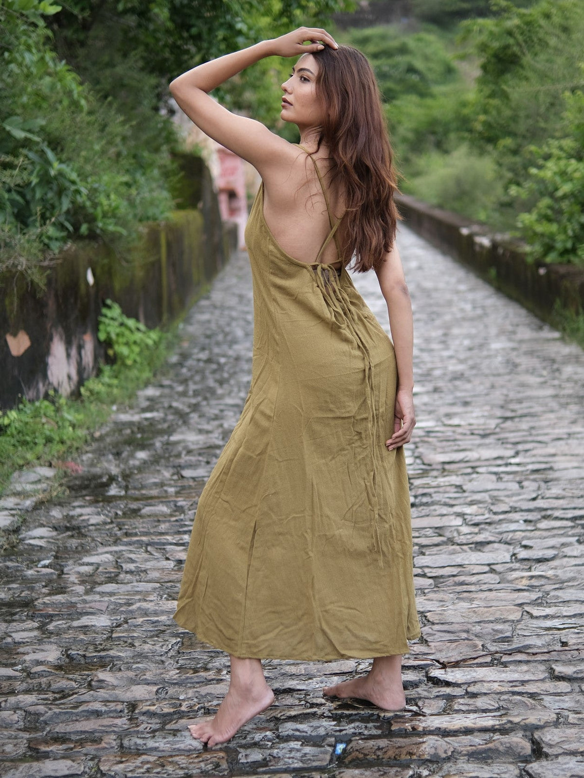 Idhika Dress in olive green, back view of the cotton maxi walking a stone path