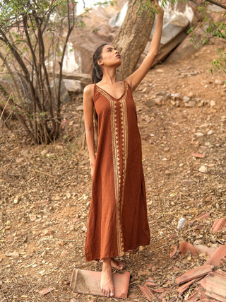Idhika Dress in rust brown, front view of the cotton maxi with arm raised against the sky