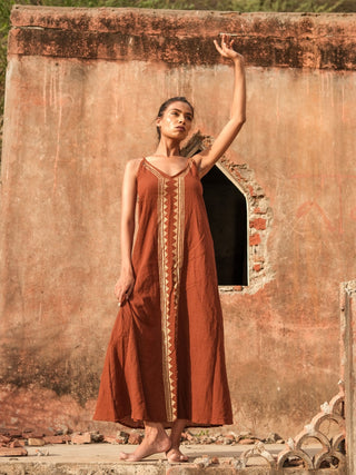 Idhika Dress in rust brown, front view of the block print cotton maxi at a weathered ruin wall