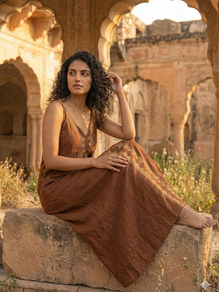 Idhika Dress in rust brown, seated view of the block print cotton maxi on a rock at golden hour