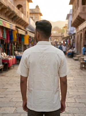 A man stands with his back to the camera in a bustling outdoor market filled with vibrant shops and colorful goods, wearing the Blossom Shirt, made from premium cotton and featuring a delicate floral block print.
