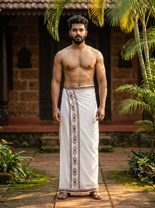 A man stands outdoors in front of a traditional building, embodying the essence of classic style as he wears the Mehfil Dhoti in Natural color. Barefoot and shirtless, he is surrounded by greenery and palm trees, showcasing an authentic ethnic look.