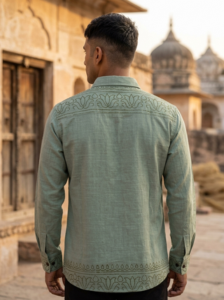 A man wearing the Madera shirt, a light green hand block print cotton piece, stands with his back to the camera in front of an old stone building with domed rooftops.