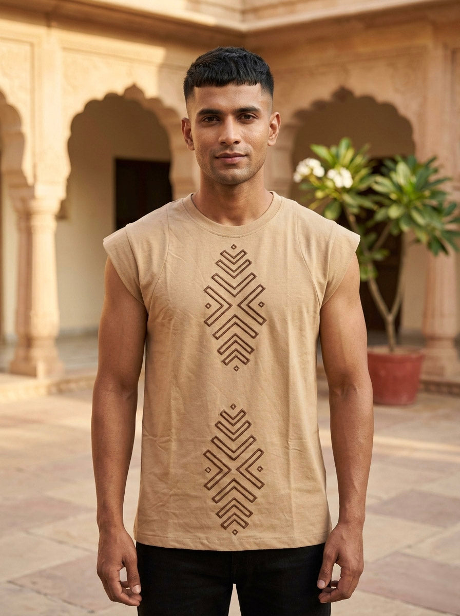 A man stands outdoors in front of an arched building, wearing the tan Ruhan Vest with Hand Block Geometric Tribal Print down the front, embodying effortless bohemian styling. There is a potted plant behind him.