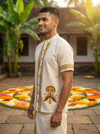 A man wearing the Arosh Shirt stands smiling outdoors, with a colorful floral rangoli design on the ground and green banana plants in the background.