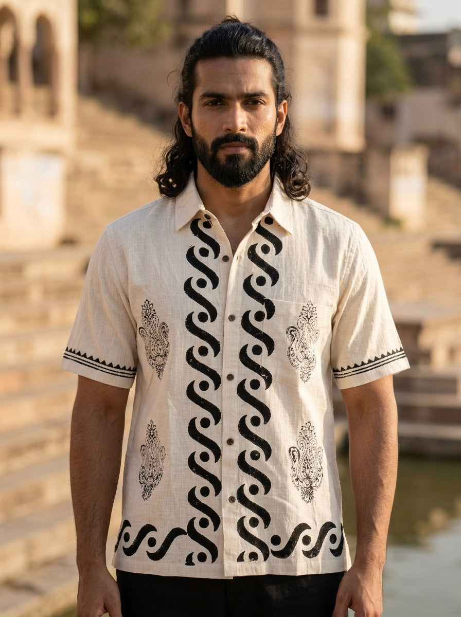 A man with long dark hair and a beard stands outdoors wearing the Natural Elio Shirt. Stone steps and historic architecture are visible in the background.