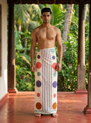 A man stands on a porch surrounded by lush green tropical plants, wearing the Naaro Dhoti in white—a unisex cotton dhoti inspired by South Indian mundu style that blends comfort with effortless flair, making it the perfect choice for stylish resort beach wear.