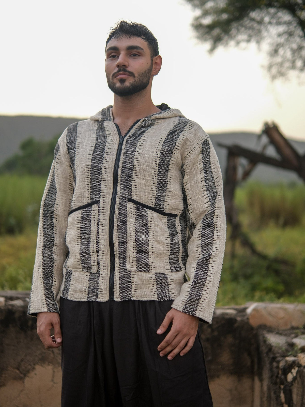 Front standing view of the striped hooded jacket with hands at the hem, showing the straight hem and stripe run