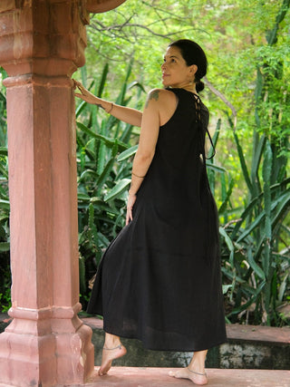Back view of the black Kashi Maxi Dress showing the laced back, beside a sandstone pillar