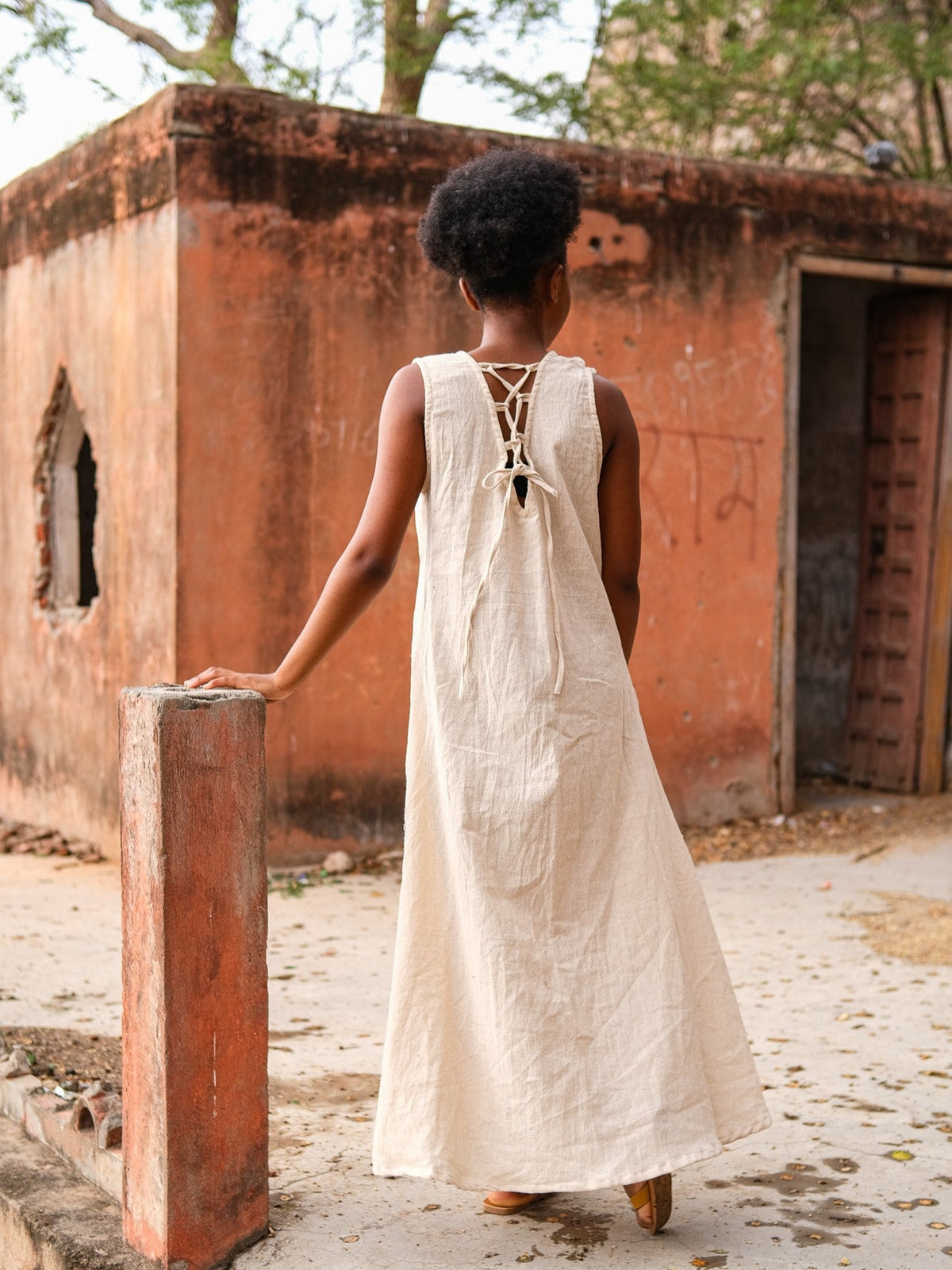 Laced back of the natural Kashi Maxi Dress, model walking past an ochre wall