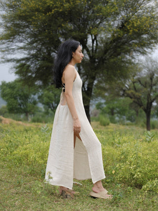 Side profile of the Kripa natural-white halter maxi dress, showing the open back tie and flowing maxi length.