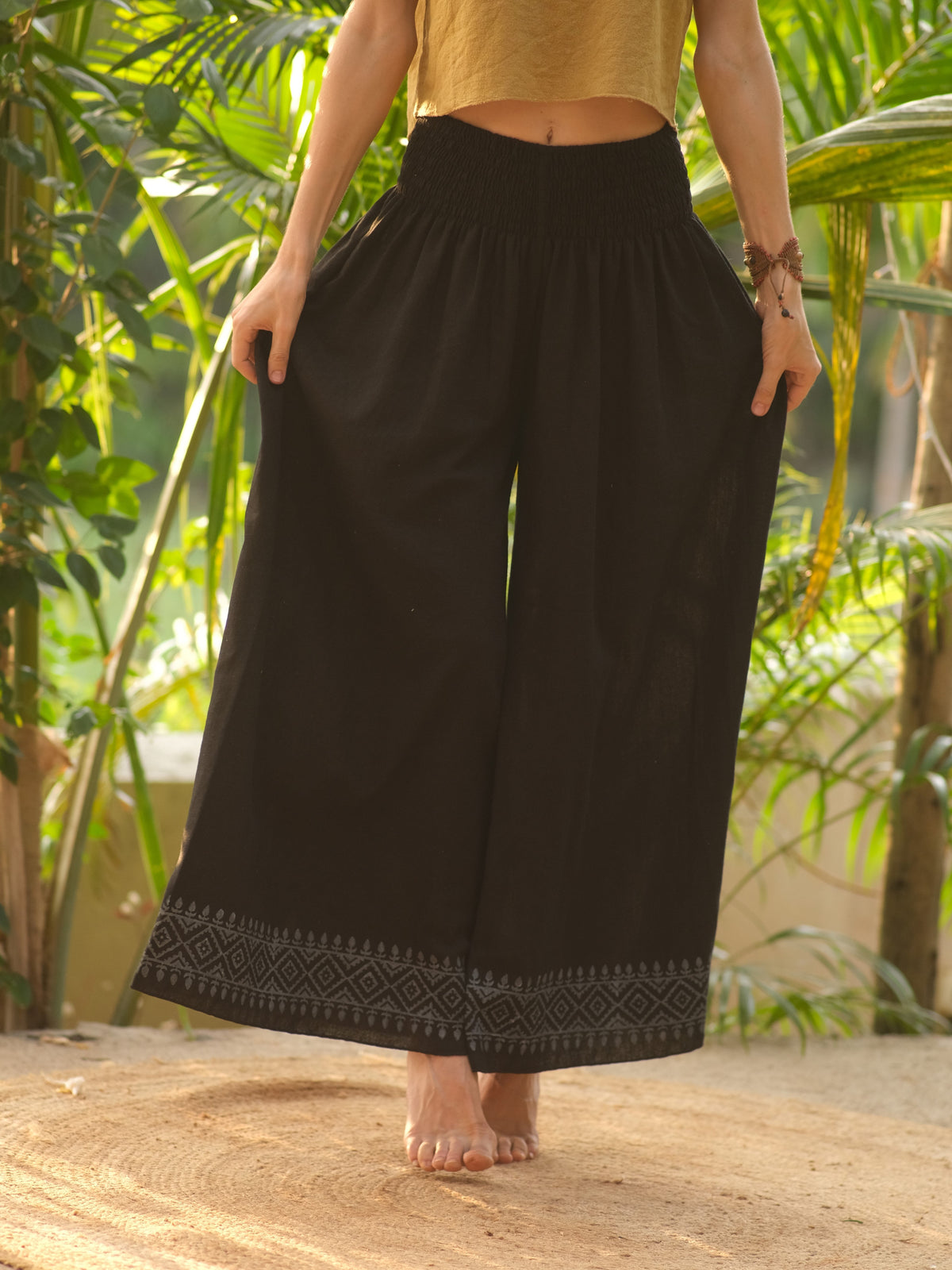 Black Medusa palazzo pants held wide at both hips to show the full leg, grey printed hem border, with a mustard crop top