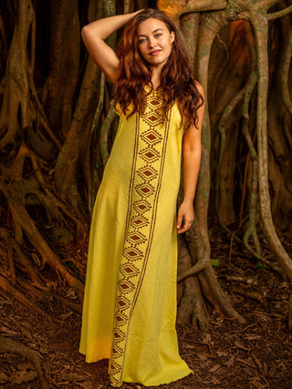 Front view of the yellow Mojo sleeveless block print cotton maxi dress with a hand raised, among banyan roots