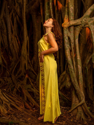 Profile view of the yellow Mojo block print cotton maxi dress with head tilted back among banyan tree roots