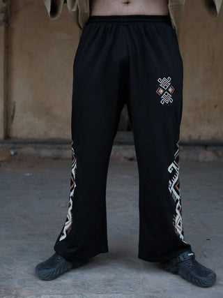 Full-length front view of black Naqsh wide-leg trousers with an ivory and copper geometric print and elasticated waist