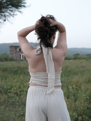 Back view of the halter top showing the open back, long self-tie knotted at the nape and smocked band, arms raised