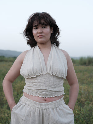 Off-white khadi cotton halter top for women, deep V neckline and smocked bodice, worn waist-up in a field