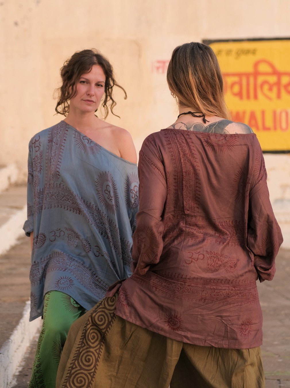 Two women in Om print kurtas, one pale grey blue and one warm brown, in a palace courtyard