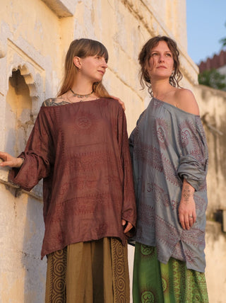 Two Om print kurtas side by side, one warm brown and one pale grey blue, against a stone wall