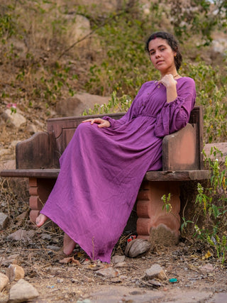 Magenta purple maxi dress with elasticated waist worn seated on a stone bench