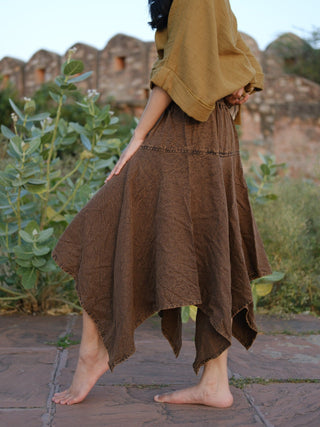 Rati Skirt brown khadi cotton falling in asymmetrical handkerchief points, stone ruin wall and greenery behind