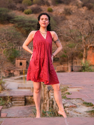 Red Om print halter cotton dress, front view with hand on hip against a heritage stone backdrop