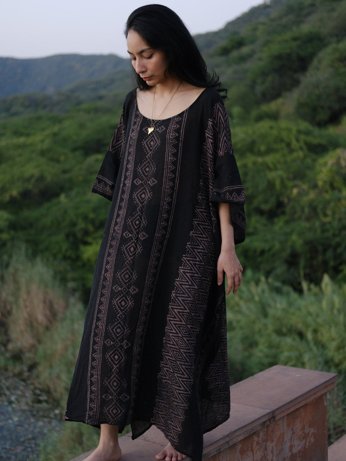 Model walking a lakeside path in the black Rooh Kaftan with wide mauve print panels