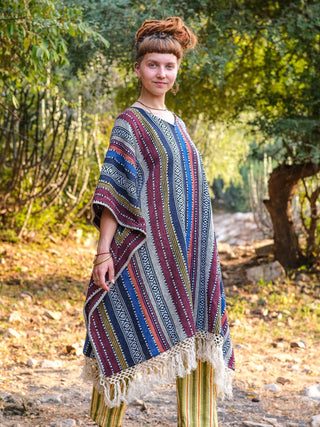 Side profile of the Saisha boho kaftan showing flowing woven stripe panels and a tasselled fringe hem