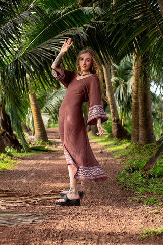 Samudra Maxi Dress brown cotton jute, model walking a red earth palm path with arm raised