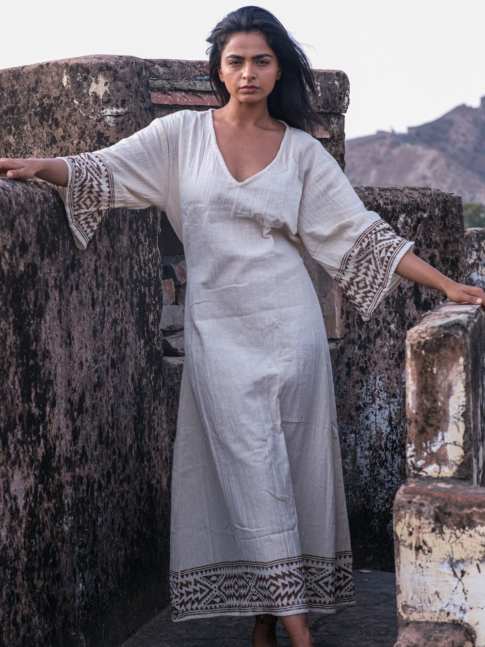 Samudra Maxi Dress natural cotton jute block print, model leaning on a fort stone wall