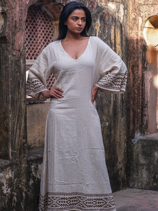Samudra Maxi Dress natural cotton jute, model hand on hip in a sunlit archway with printed hem