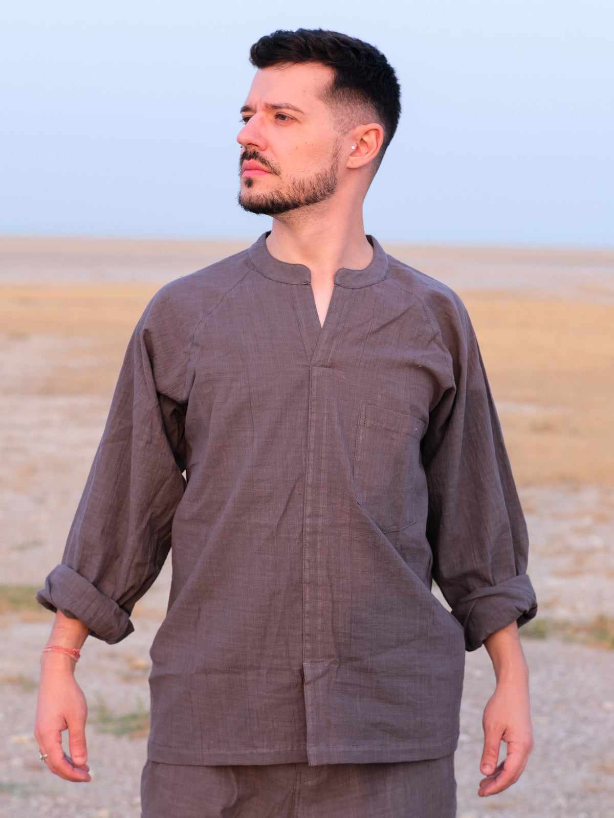 Man wearing the Shlok Kurta in grey cotton, mandarin collar and open placket, standing in an open field.