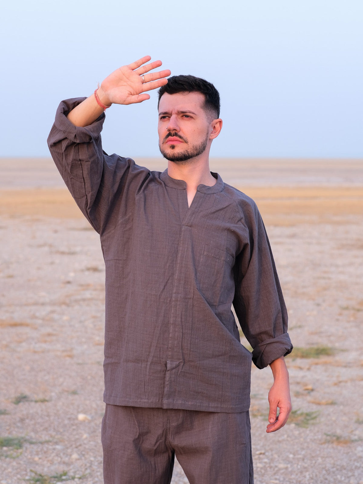 Shlok Kurta in grey cotton, loose unisex fit, worn with one hand raised shielding the sun.