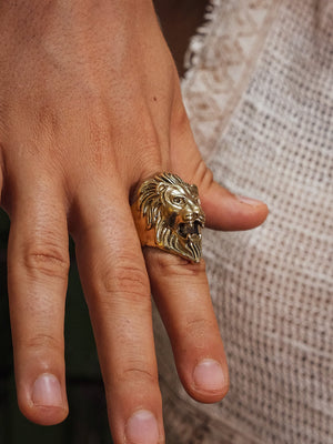 Close-up of the Singam brass lion head ring worn on a finger against a cream crochet top