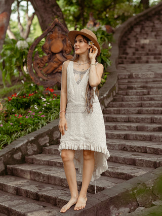 Surekha white lace dress styled with a wide hat, standing on carved wooden steps in a garden